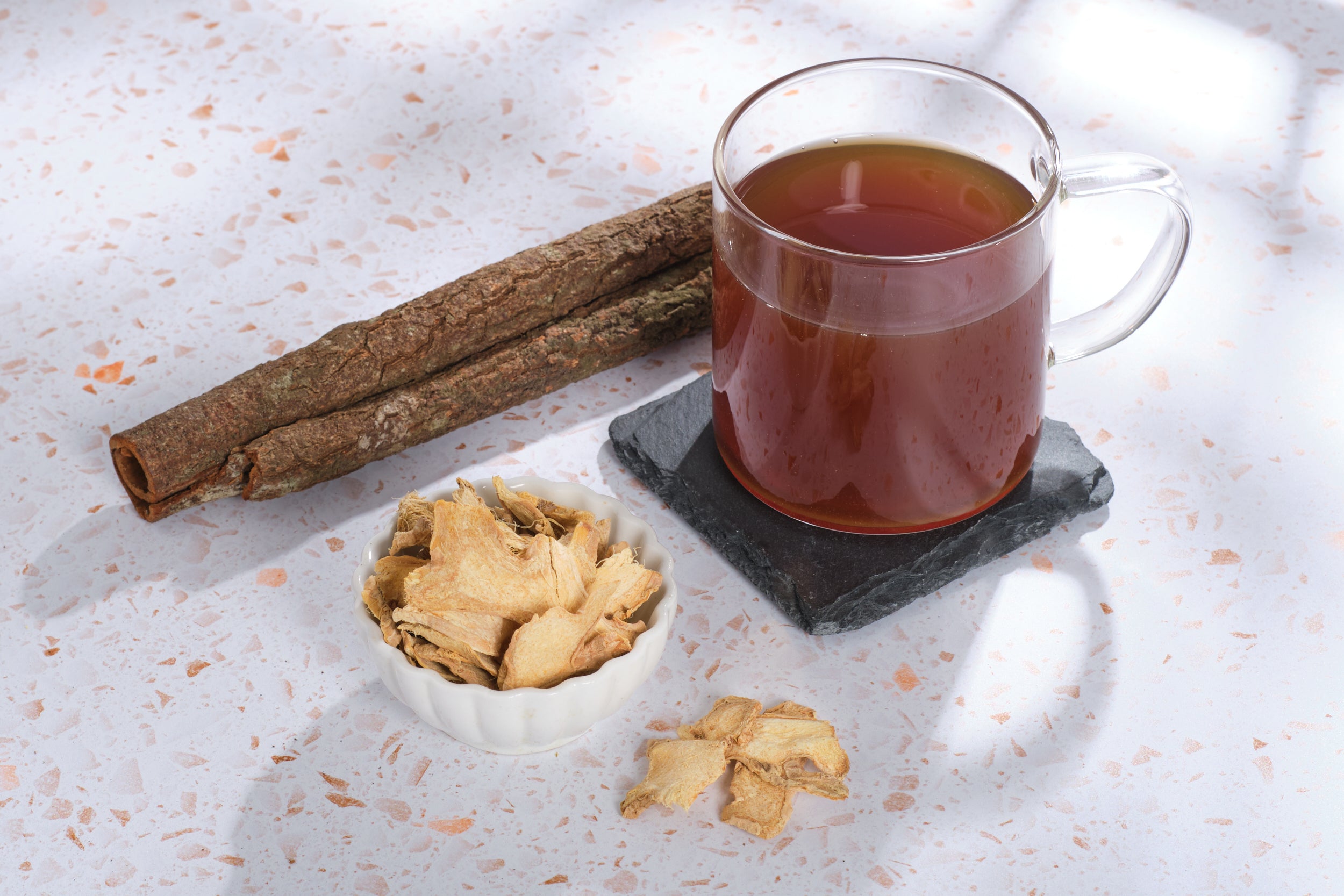 The ingredients of Atomic Fungi Functional Mushroom Focus Elixir's tea around a cup of the tea, against a white tabletop.