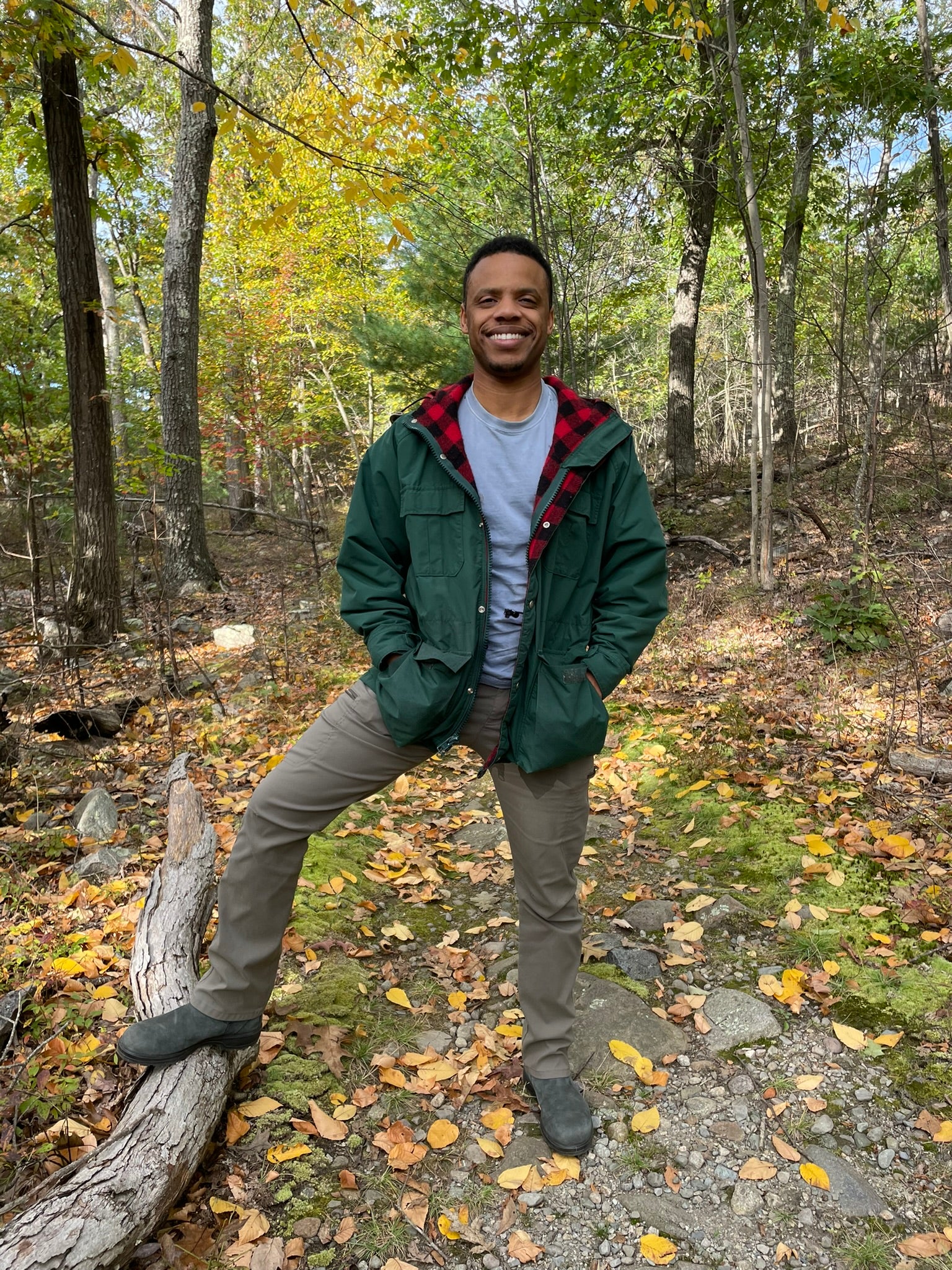 Atomic Fungi Founder, Giovanni, out hiking in the woods while looking at mushrooms and wearing a green jacket with a red checkered inner lining.